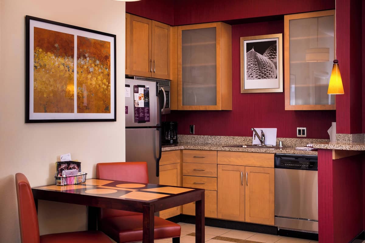 A compact kitchen with wooden cabinets, a stainless steel refrigerator, a coffee maker, and a dishwasher.