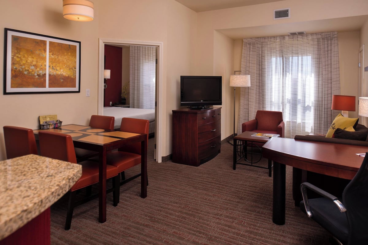 A hotel room with a dining area, a TV, and a seating area with a view of the city.