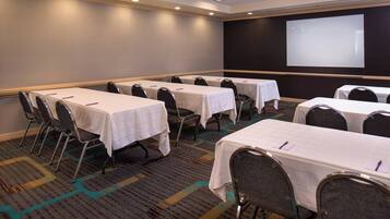 A conference room with multiple tables and chairs, a projector screen, and carpeted flooring.