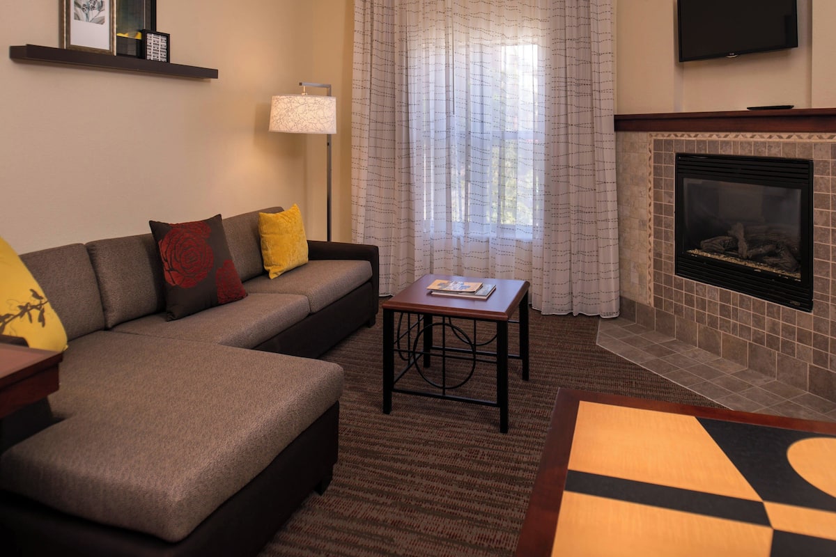 A living room with a sectional sofa, a small table, a fireplace, and a TV mounted on the wall.