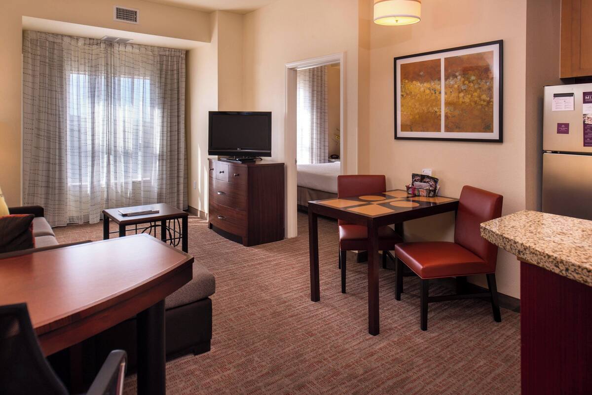 A hotel room with a dining area, a television, a refrigerator, and a window with curtains.
