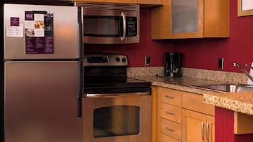 Una cocina con electrodomésticos de acero inoxidable, armarios de madera, encimeras de granito y salpicadero rojo.