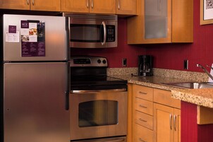 Una cocina con electrodomésticos de acero inoxidable, armarios de madera, encimeras de granito y salpicadero rojo.
