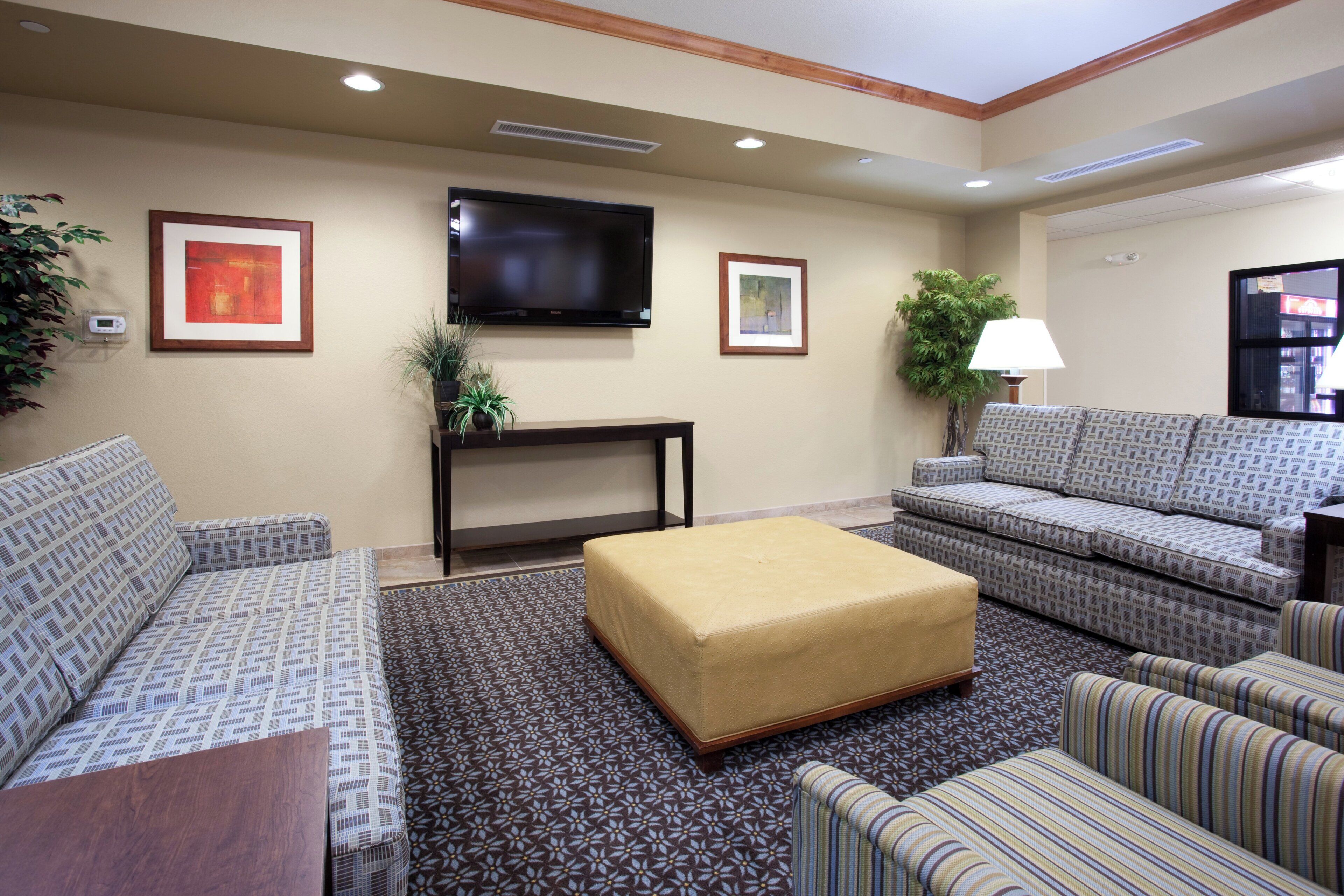 A hotel room with a sofa set, a flat-screen TV, a small table, and a lamp.