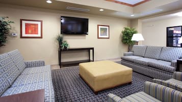 A hotel room with a sofa set, a flat-screen TV, a small table, and a lamp.