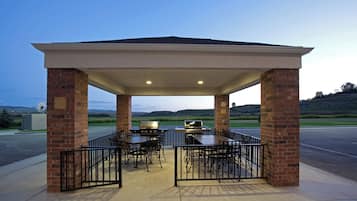 A covered outdoor seating area with brick pillars, tables, and chairs, overlooking a scenic landscape.