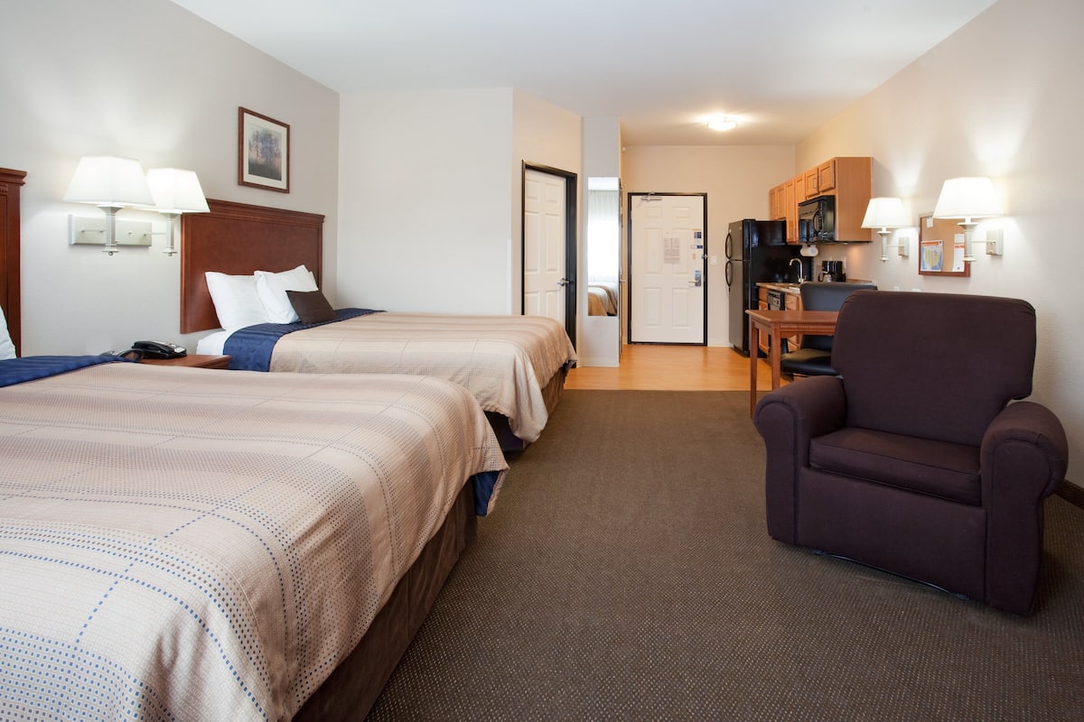 A hotel room with two beds, a dining table, a kitchen area, and a seating area.