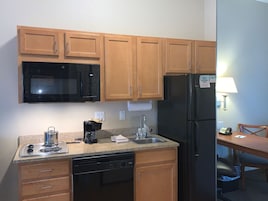 Una cocina compacta con armarios de madera, un microondas negro, un refrigerador negro, una cafetera y un lavamanos.