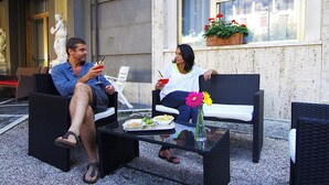 Deux personnes sont assises sur des chaises en osier, autour d’une table en verre, devant des assiettes remplies de nourriture et des boissons.