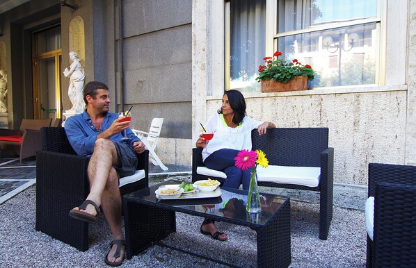 Two people seated on wicker chairs at a glass table with plates of food and drinks. - Grand Hotel Milano (Chianciano Terme)
