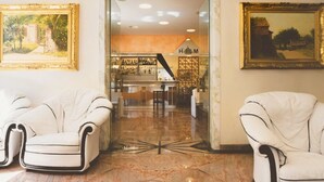 Un hall d’entrée avec deux fauteuils à accoudoirs en cuir blanc, un sol en marbre et un bar situé au fond de la pièce.