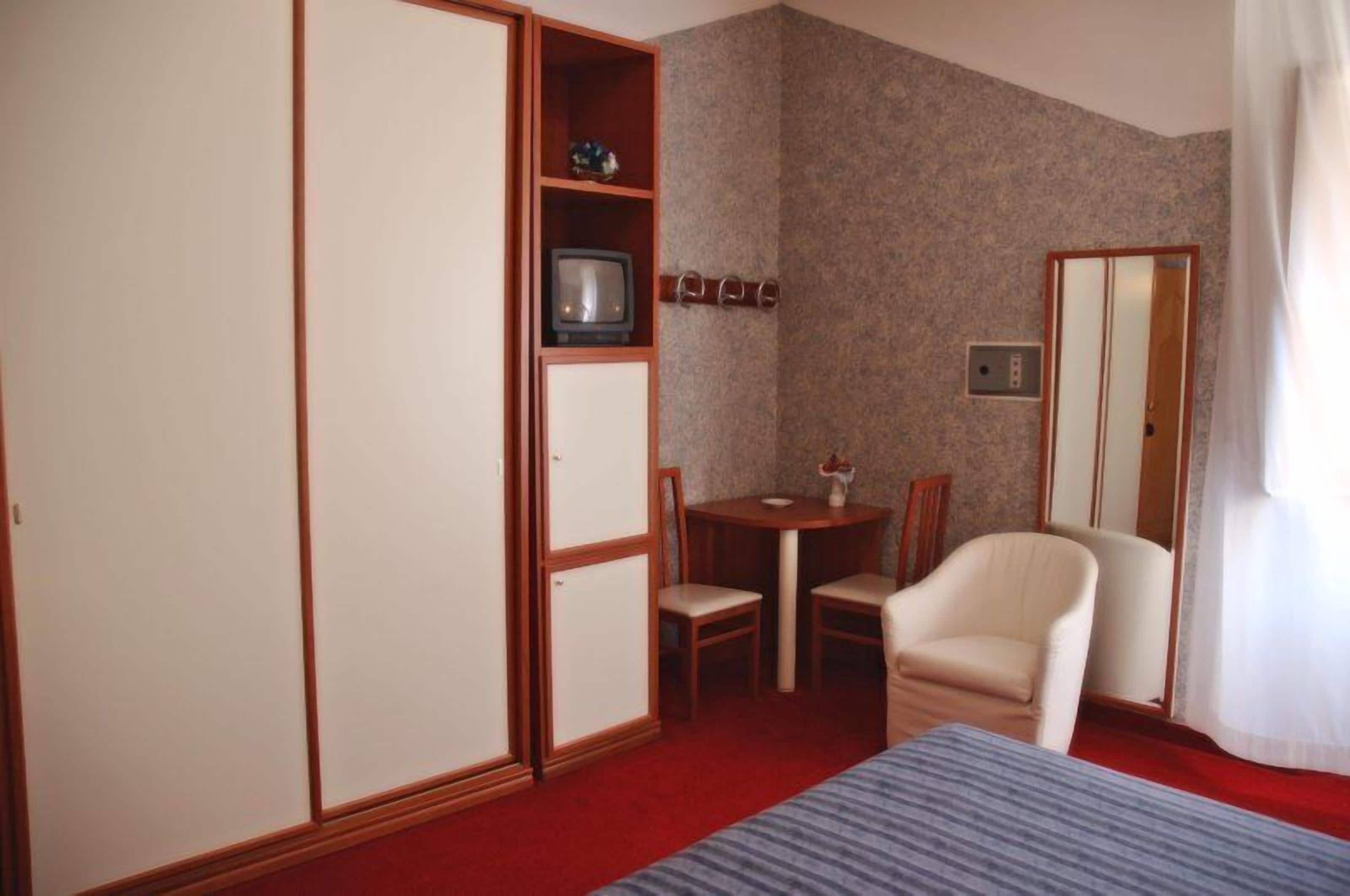 Una camera d'albergo con un letto, una scrivania con una sedia, una televisione e un armadio.