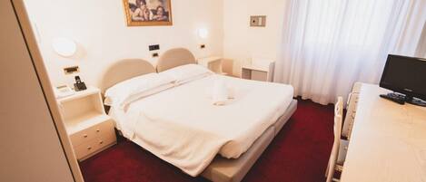 A hotel room with a bed, bedside tables, a desk, a chair, and a television.
