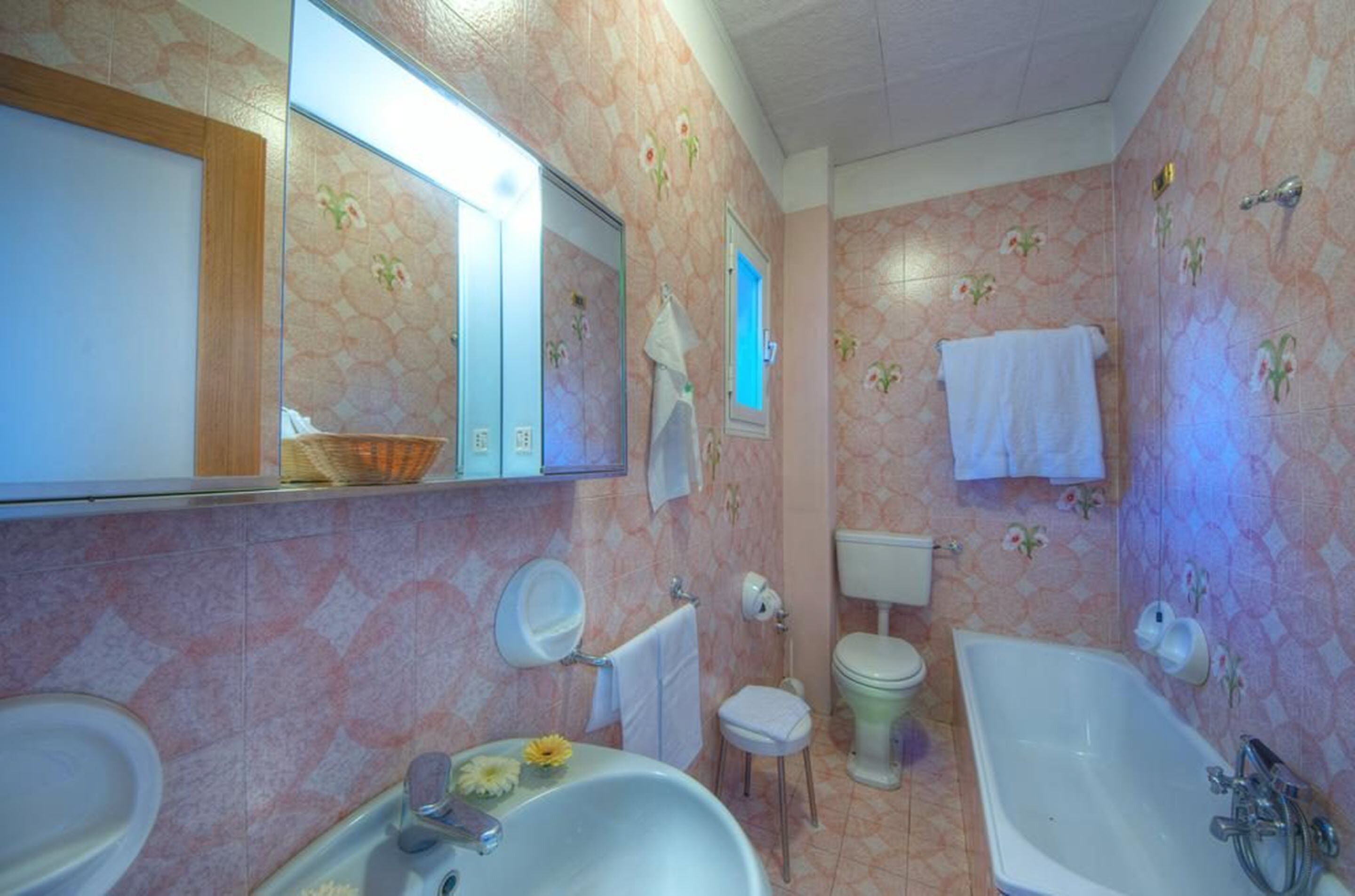 Une salle de bain équipée d’un lavabo, de toilettes et d’une baignoire, avec un papier peint à motifs floraux et un miroir au-dessus du lavabo.