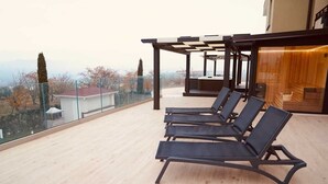Une terrasse sur le toit avec quatre fauteuils noirs, une balustrade en verre et une plateforme en bois.