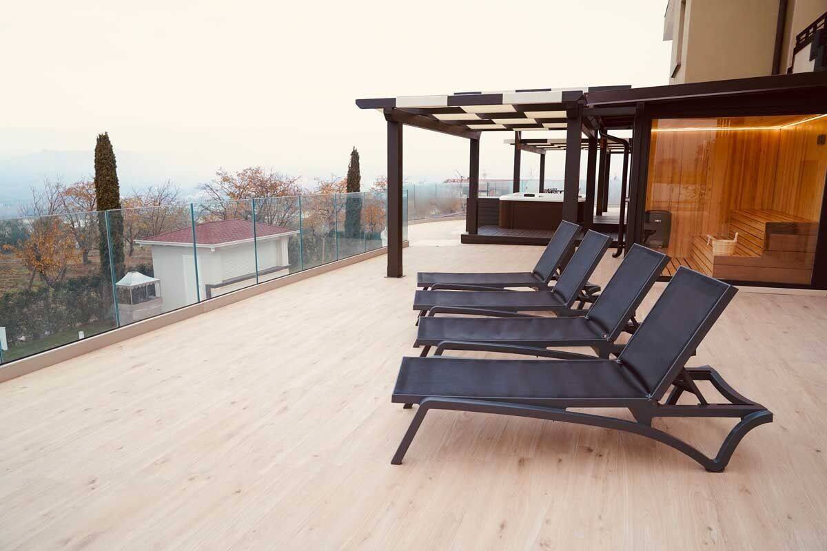 Una terraza en la azotea con cuatro sillones de lounge negros, una barandilla de cristal y una cubierta de madera.