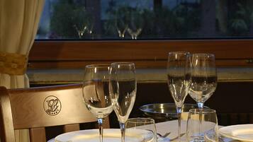 Mesa de comedor dispuesta con copas de vino, platos y cubiertos, con vista a una montaña y un edificio al fondo.