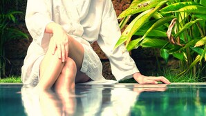 Une personne assise au bord d’une piscine, avec une végétation luxuriante en arrière-plan.