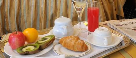 Une chambre d’hôtel avec un lit soigneusement fait, un plateau contenant des articles pour le petit-déjeuner, notamment des fruits, un croissant et des boissons, ainsi qu’un tableau accroché au mur.