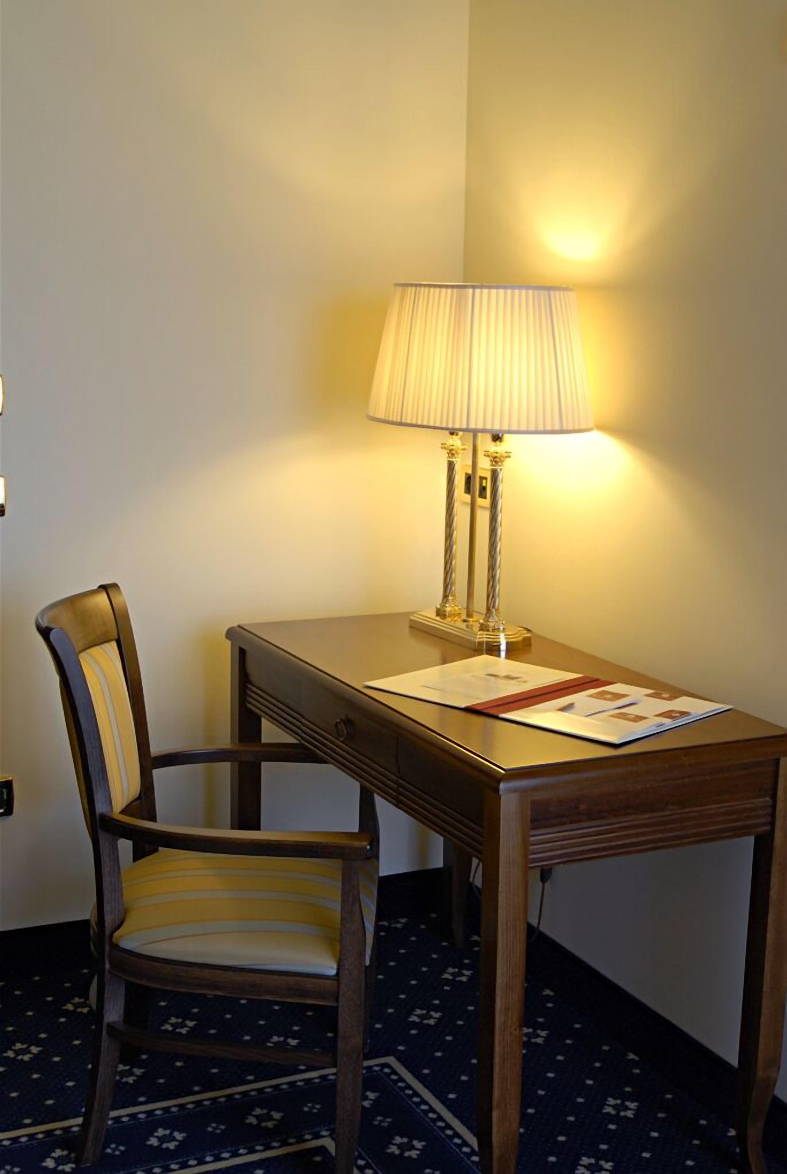 A wooden desk with a lamp and papers, a striped chair, and a carpeted floor.