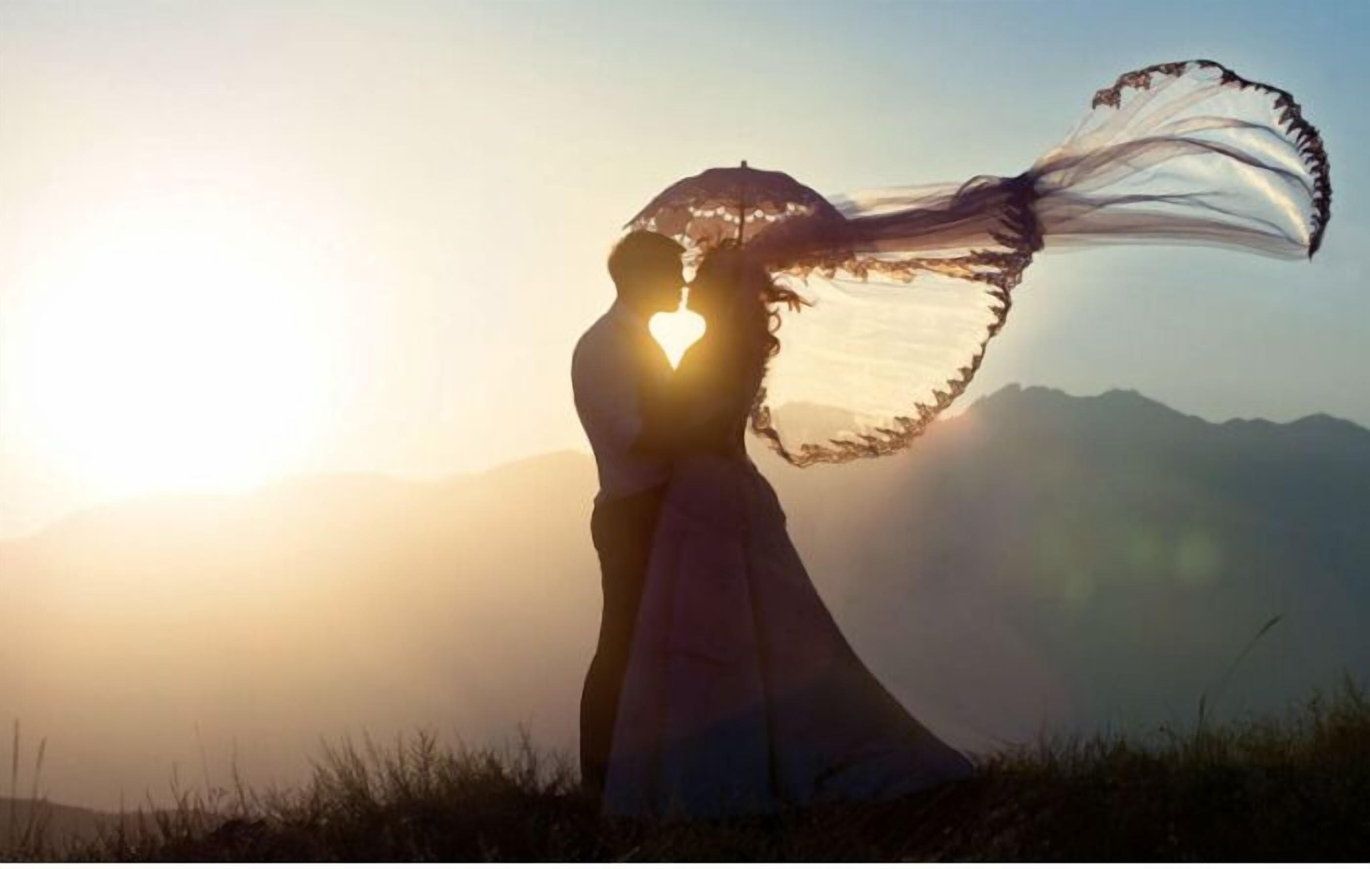 Una pareja abrazada con una silueta en forma de corazón al atardecer.