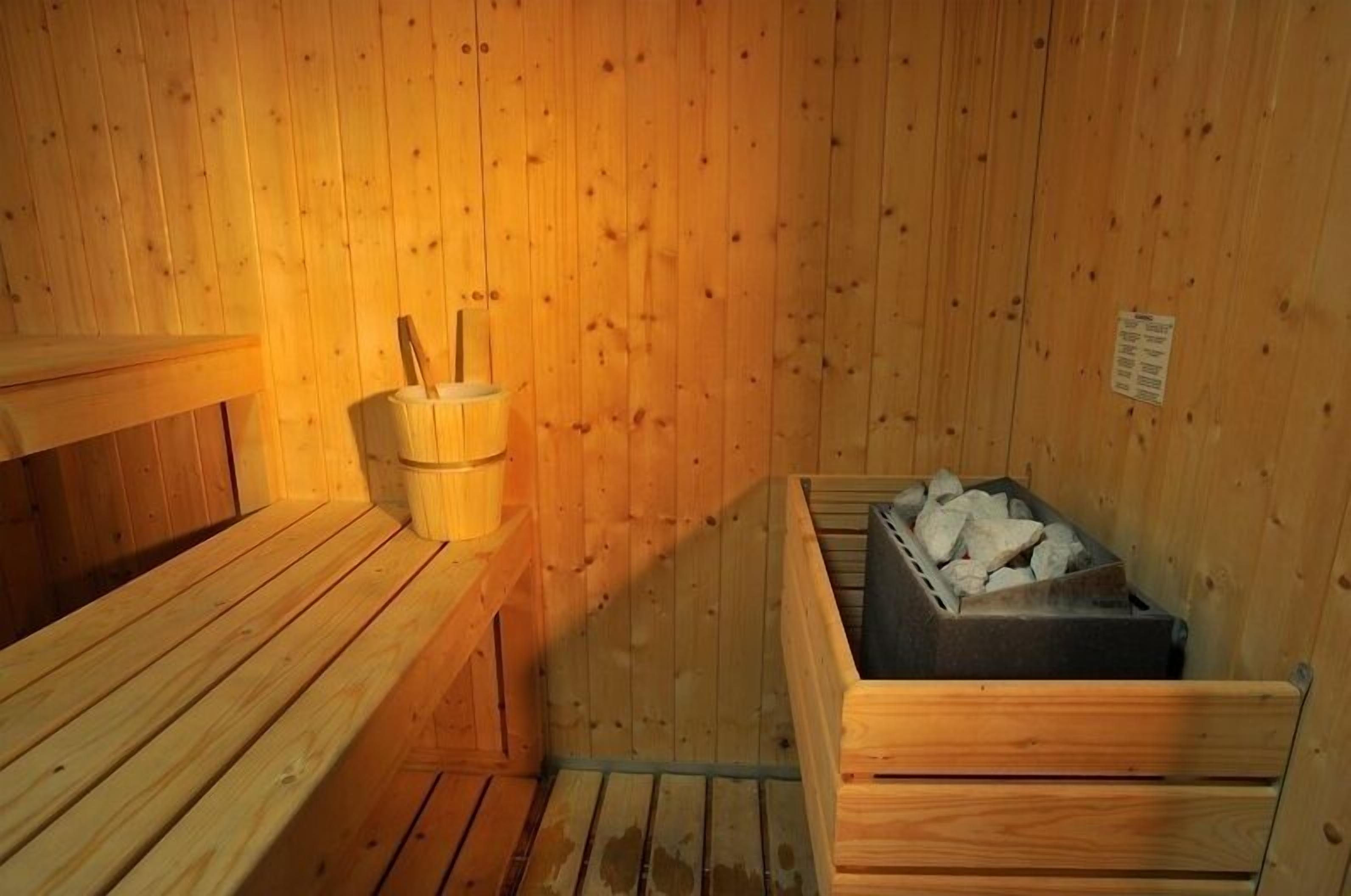 Una sauna de madera con bancos y un recipiente lleno de piedras, probablemente para calentar.