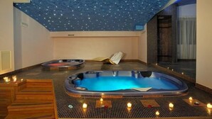 Une salle de spa dotée d’un grand bain à remous, de sièges en bois et de bougies.