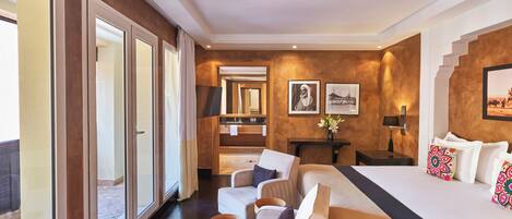 Habitación de hotel con una cama grande, dos sillones, una mesita, un escritorio y vistas al exterior.