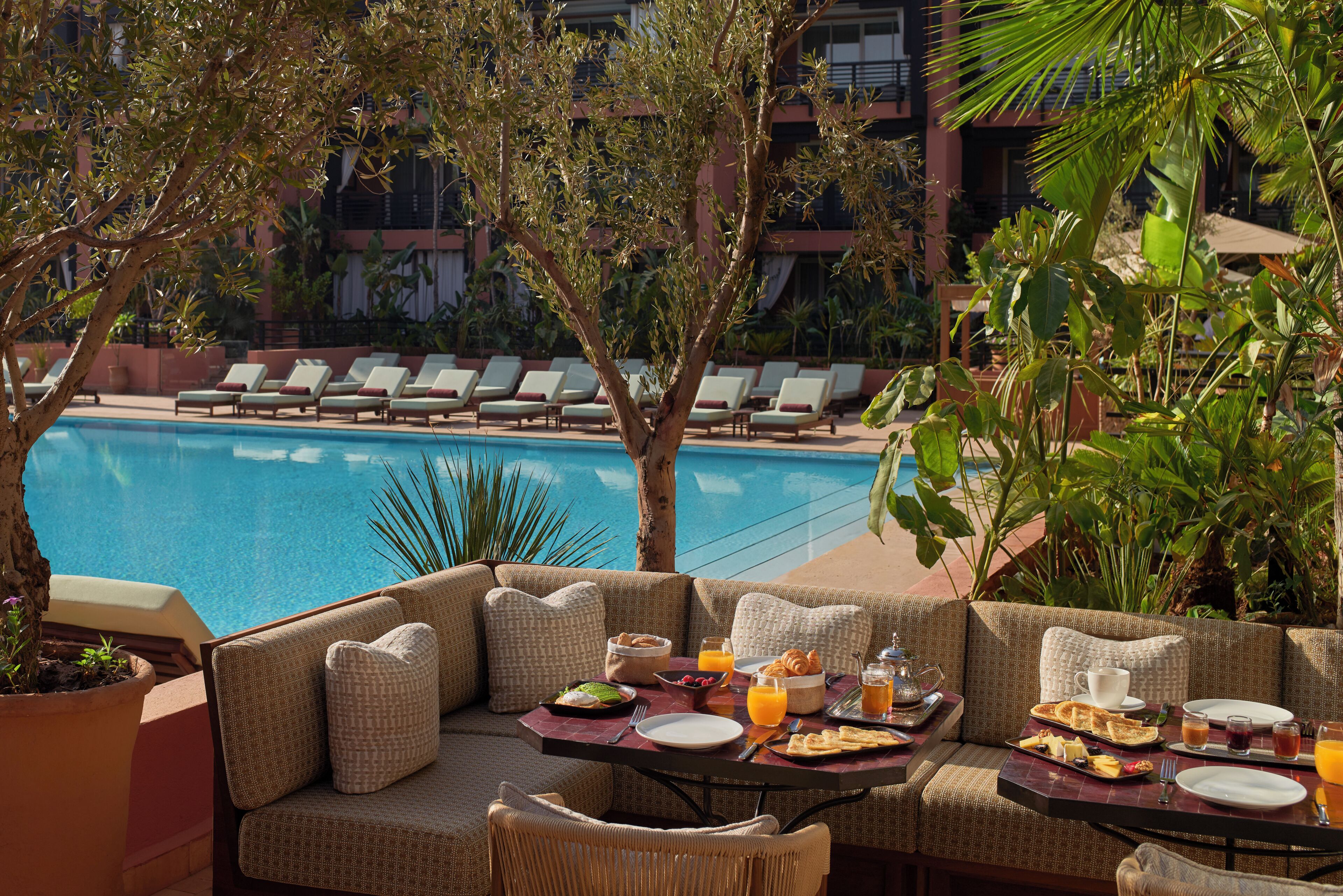 A poolside seating area with a table set for breakfast, overlooking a swimming pool.