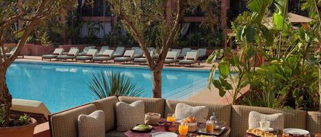 A poolside seating area with a table set for breakfast, overlooking a swimming pool.