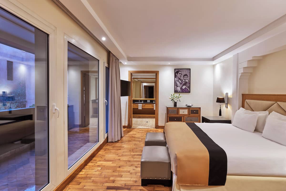 A modern hotel room with a large bed, a seating area, a bathroom, and a view through a glass door.