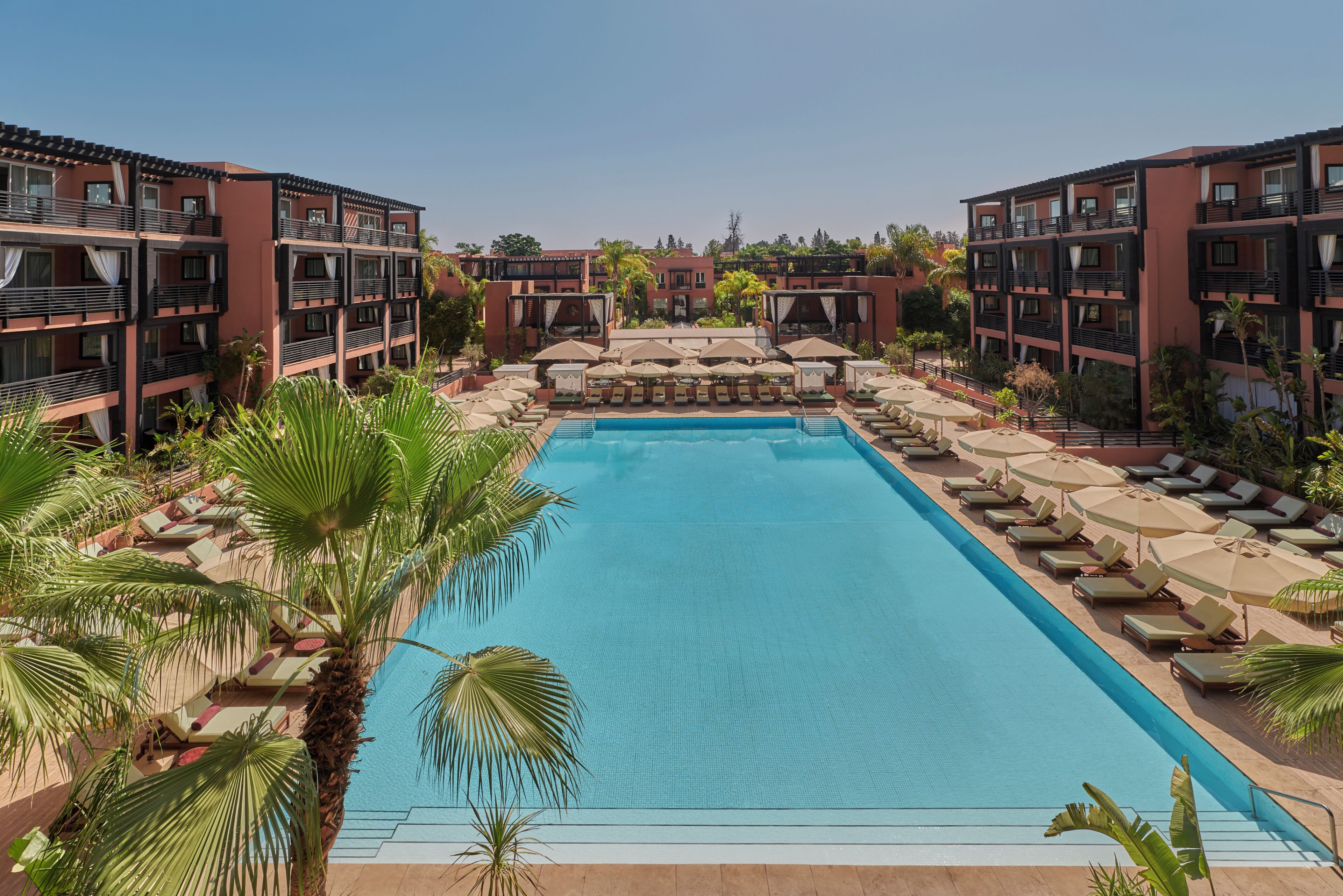 A swimming pool with lounge chairs and umbrellas, surrounded by multi-story buildings with balconies.