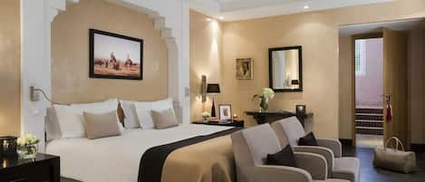 A hotel room with a large bed, two armchairs, a nightstand, and a desk.