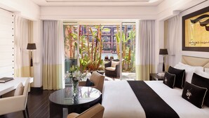 A hotel room with a large bed, a dining table, and a view of a pool area.