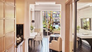 A modern hotel room with a dining area, a seating area with a view of the pool, and a large sliding glass door leading to the outdoor space.