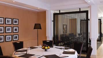 Zona pranzo con tavolo rotondo apparecchiato per sei persone, circondato da sedie. Si notano quadri appesi al muro, un divisorio nero e una lampada.