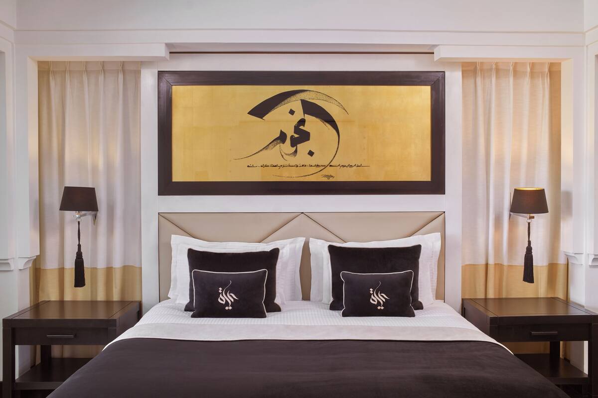 A hotel room with a large bed, two nightstands, a headboard with a framed artwork, and curtains.