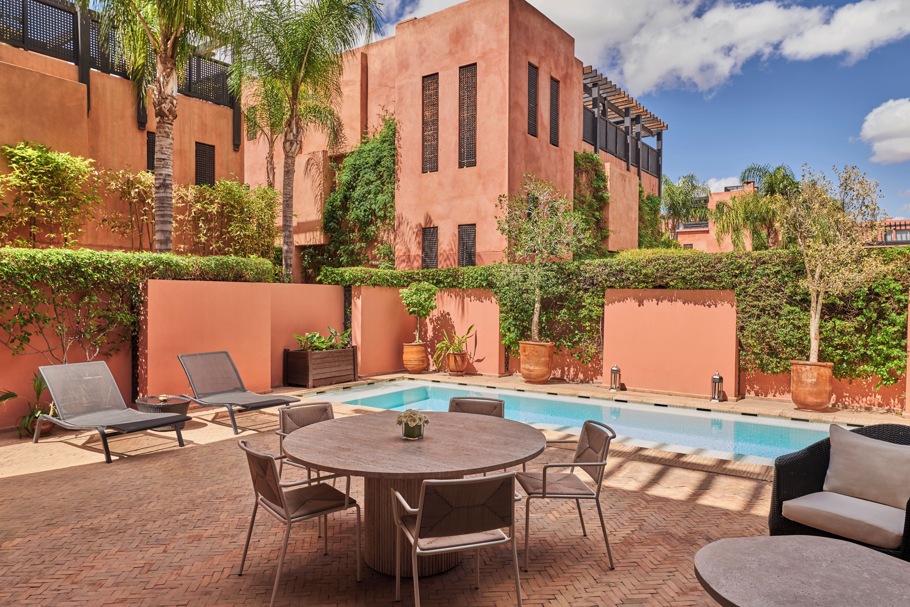 A poolside area with a round table and chairs, lounge chairs, and a swimming pool.