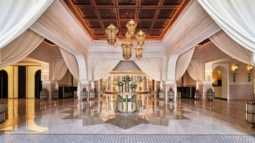 Un hall espacioso con techo alto, candelabros ornamentales y una mesa central con arreglos florales.