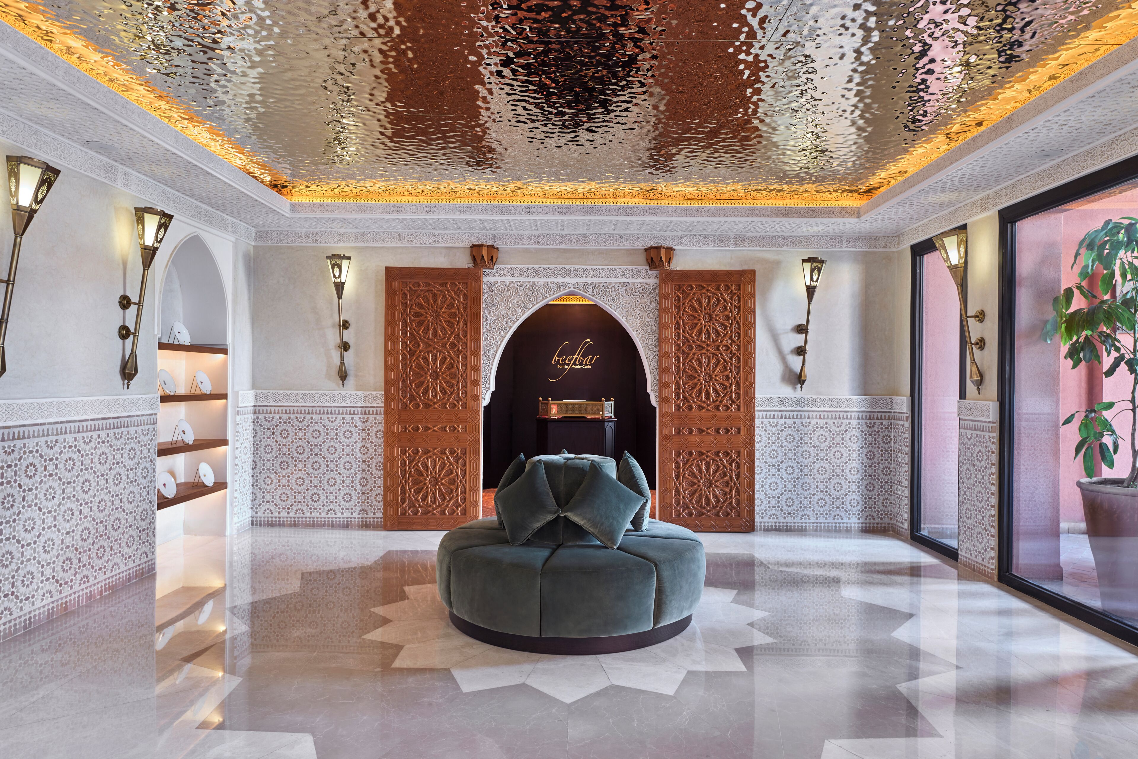 Un interno lussuoso con una zona salotto centrale, pannelli murali decorati e un soffitto ricco di motivi intricati.