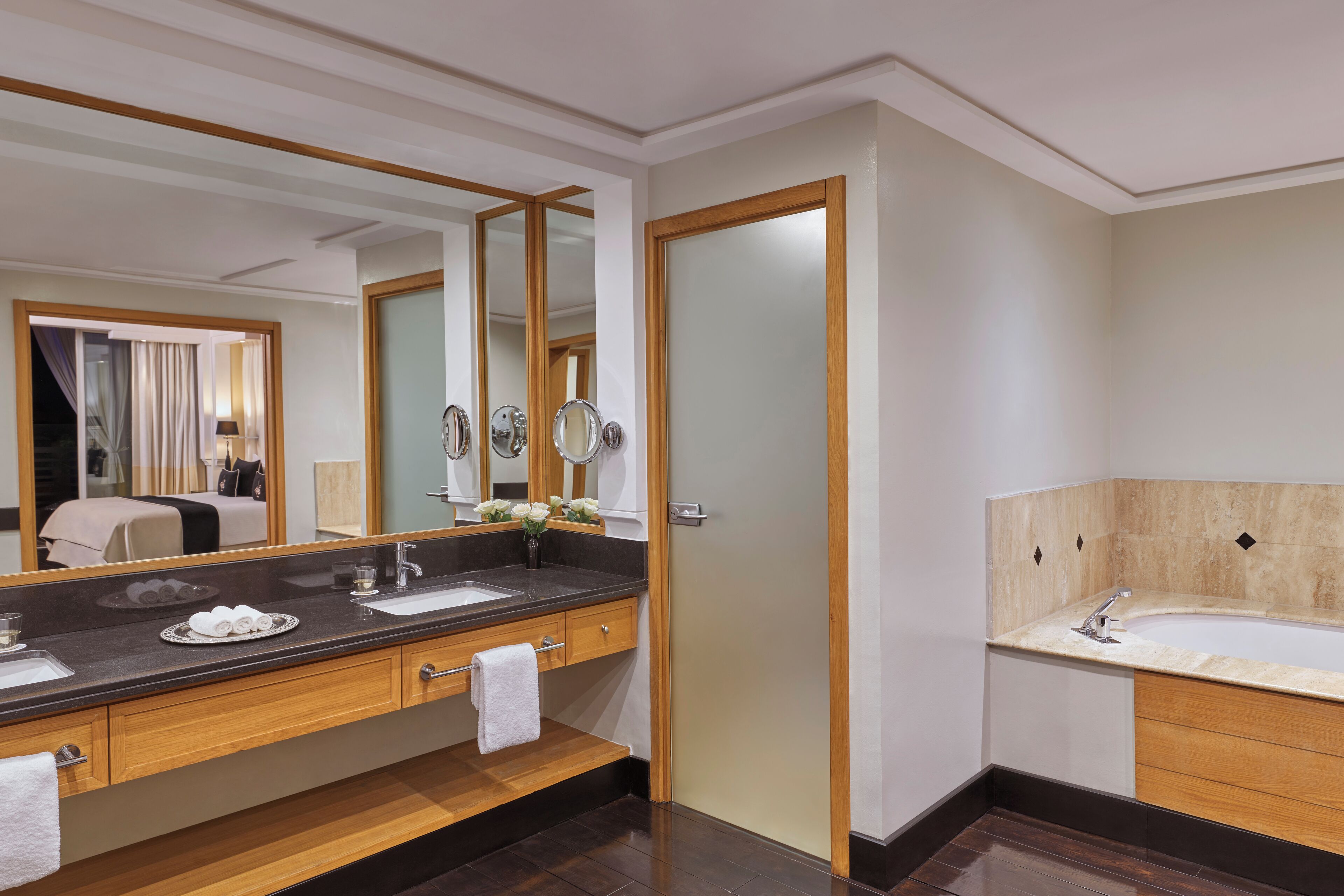 A modern bathroom with a large mirror, wooden vanity, and a separate bathtub area.