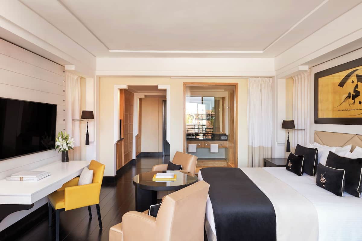 A modern hotel room with a large bed, a sofa, a dining table, and a TV.