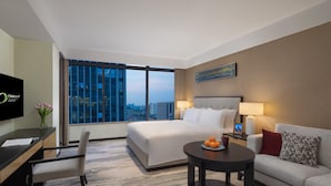 A hotel room with a large bed, a desk, a chair, a sofa, a coffee table, and a TV.