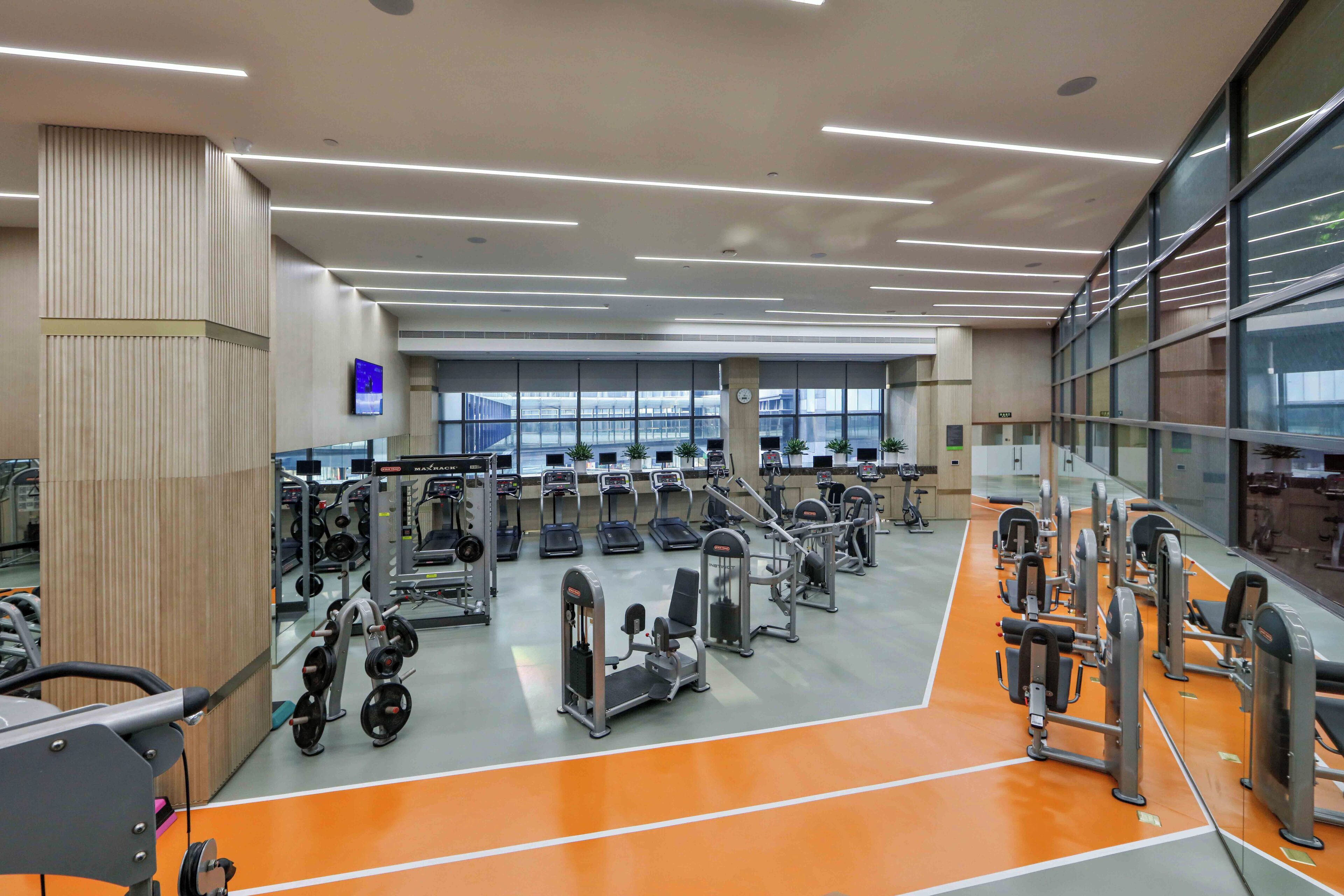 Un gimnasio con diverso equipamiento de ejercicio, un ventanal grande y un diseño de techo moderno.