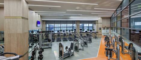 Un gimnasio con diverso equipamiento de ejercicio, un ventanal grande y un diseño de techo moderno.