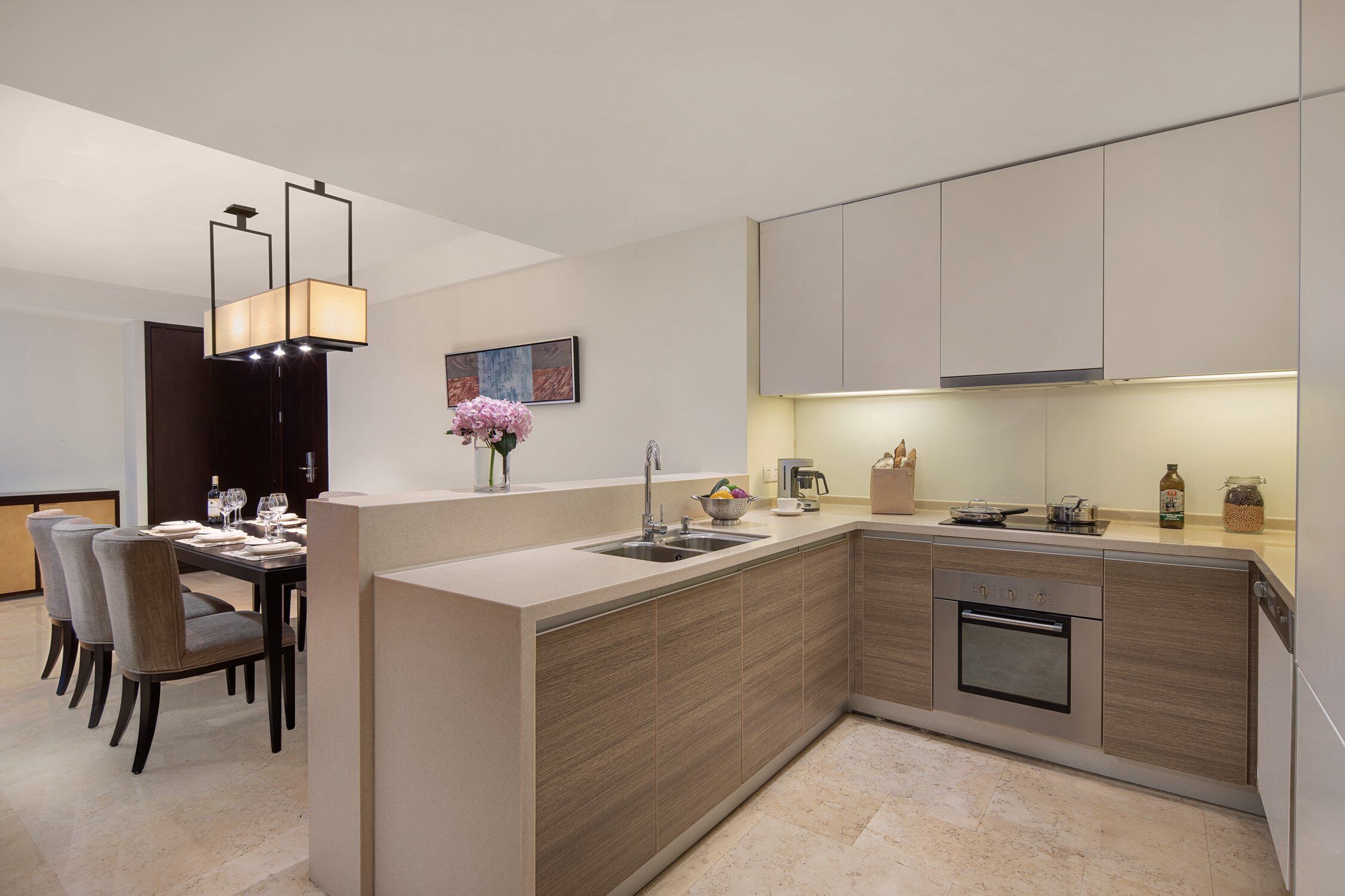 Een moderne keuken met een centraal eiland, een inbouwoven en een eethoek met stoelen en een tafel.