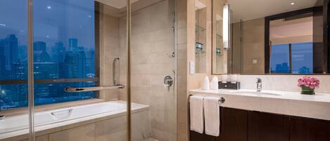 Un baño moderno con cabina de ducha de vidrio, un ventanal con vistas a la ciudad, un tocador con espejo y un lavabo.
