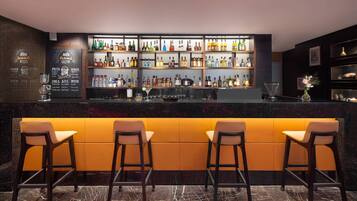 Zona de bar con suelo de mármol, tres taburetes y estantes llenos de botellas de licores.