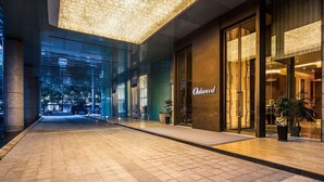 Una entrada de hotel moderna con fachada de vidrio, un techo grande iluminado y un interior bien iluminado.
