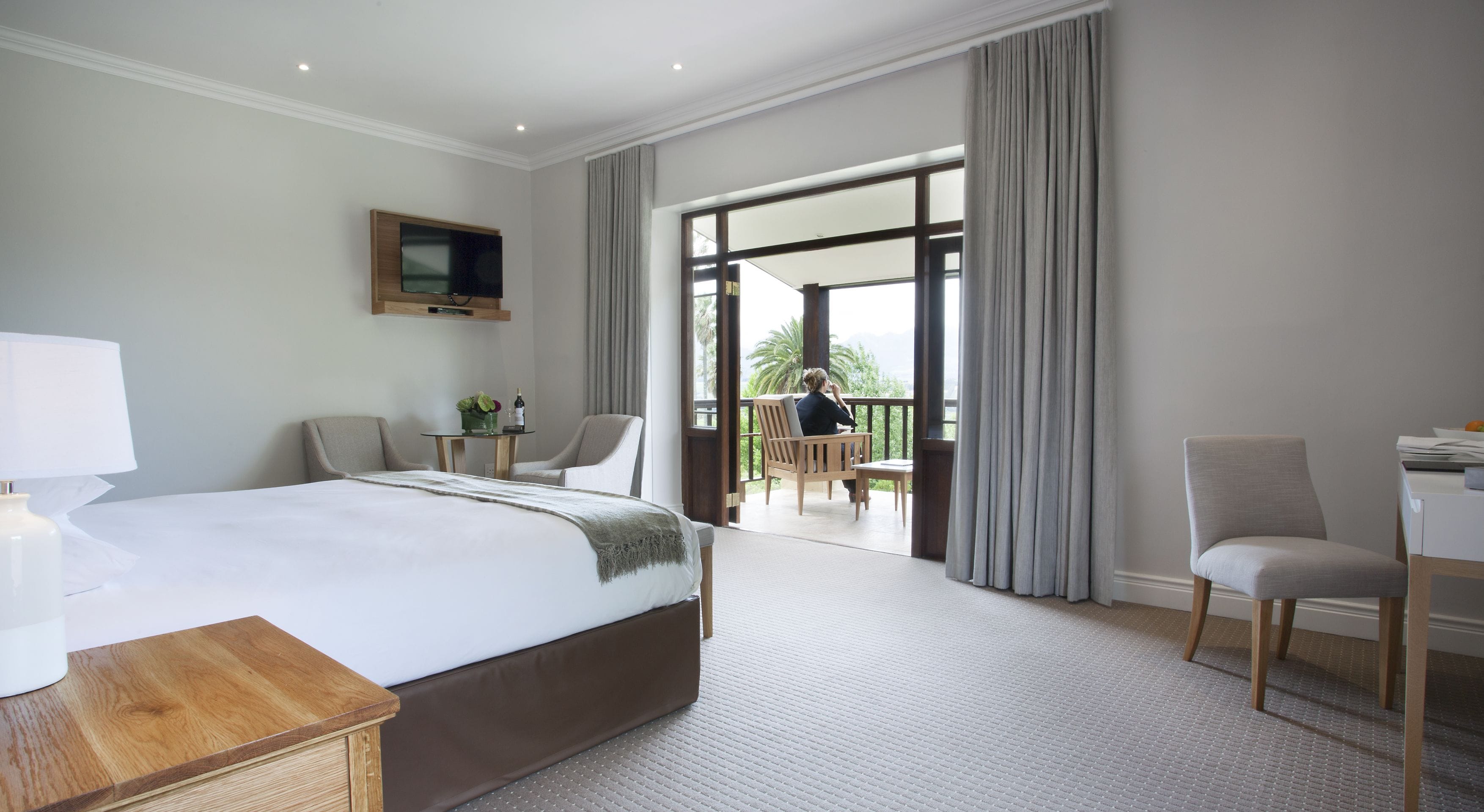 Een hotelkamer met een groot bed, een bureau, twee stoelen, een televisie en een balkon met uitzicht.